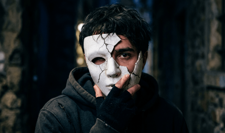 Person holding a cracked white mask to face with one eye showing