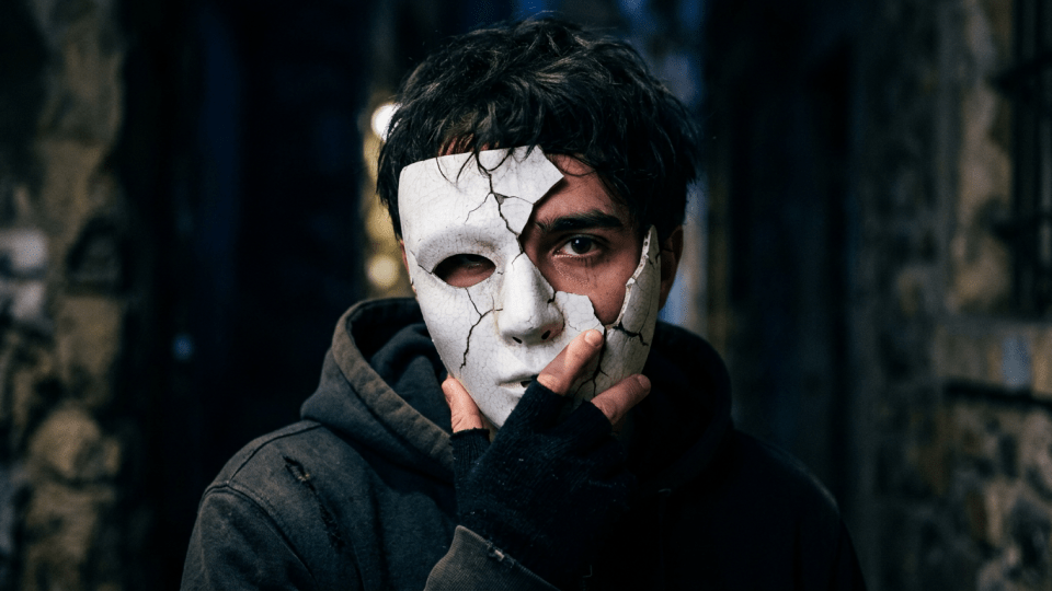 Person holding a cracked white mask to face with one eye showing
